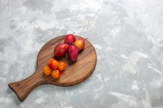 Half-top view different formed plums sour and fresh fruits on light-white desk.