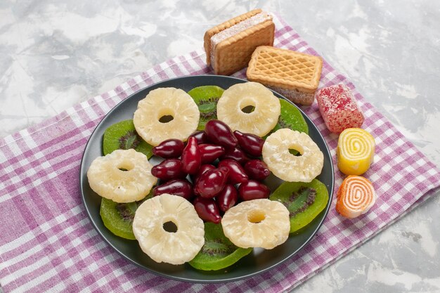 Вид сверху на сушеные фрукты, ананасовые кольца, кизил, вафли и ломтики киви на белом столе