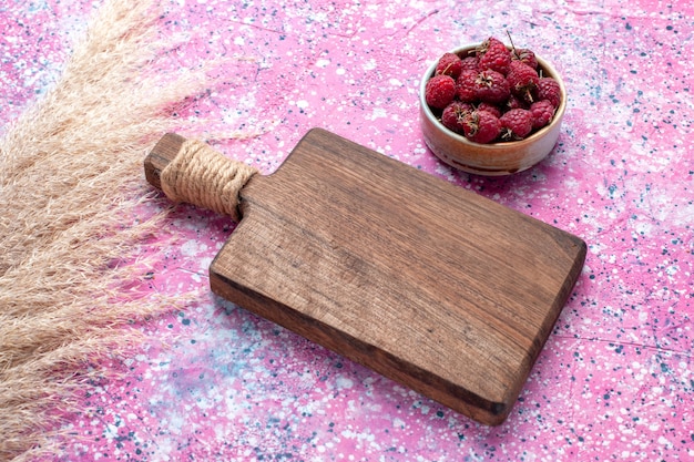 Half-top view of fresh tasty raspberries inside white plate on pink surface