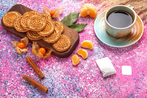 Половина сверху круглое сладкое печенье вкусное маленькое печенье с чашкой чая и мандаринами на розовом столе.