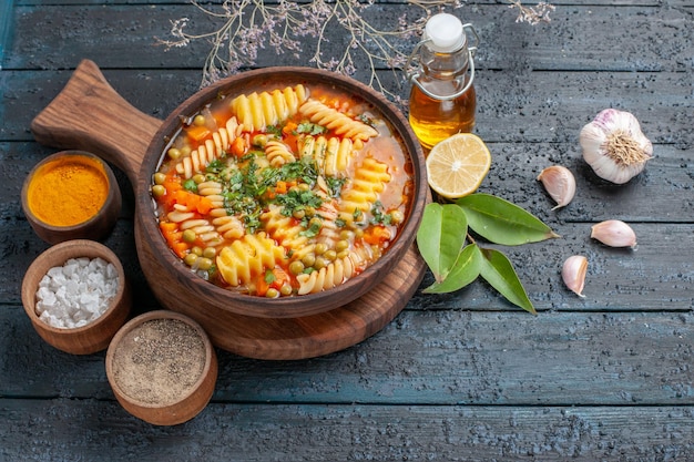 Zuppa di pasta a spirale con vista a metà dall'alto pasto delizioso con diversi condimenti sulla cucina di piatto di pasta italiana di colore blu scuro