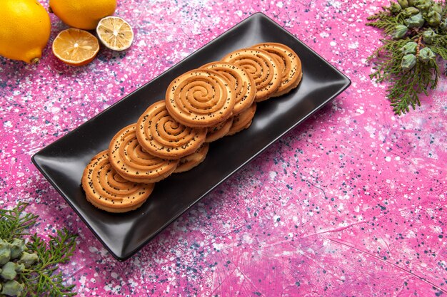 ハーフトップビューの甘いクッキーライトピンクの机の上にレモンが入った黒い形の中においしい小さなクッキー。