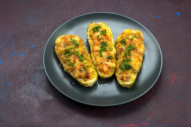 Half-top view tasty baked squashes with greens inside plate on dark background.