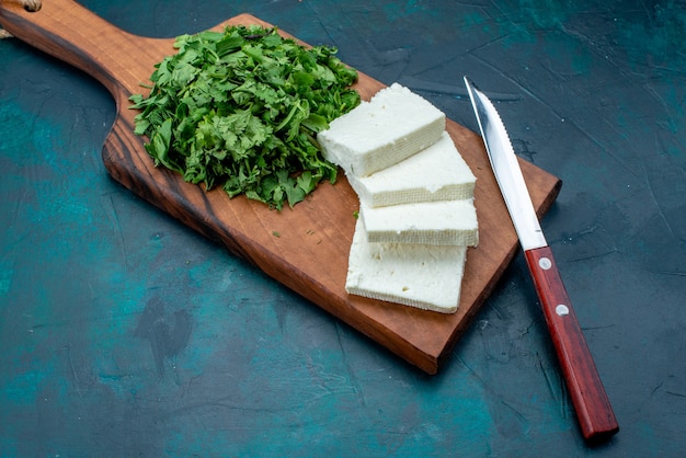 Half-top view white cheese with fresh greens on dark-blue background.