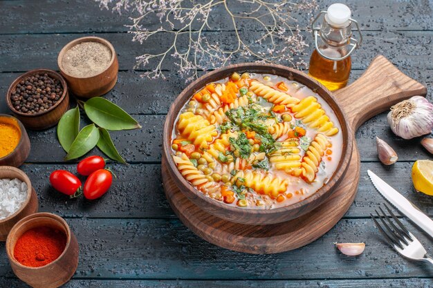 Вкусный суп из макаронных изделий из спиральных итальянских макарон с приправами на темно-синем столе, вид сверху, паста суп цветное блюдо ужин кухня