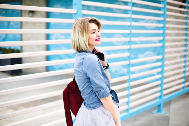 Half-turned beautiful woman with bright pink lips holding smartphone looking to her left