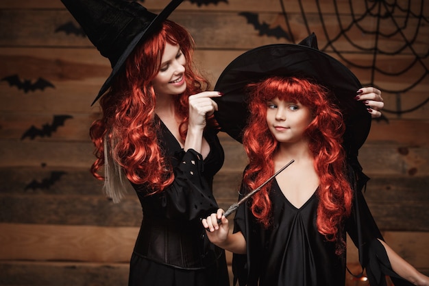 Концепция Хэллоуина красивая кавказская мама одевается для своей дочери в костюмы ведьмы и длинн ...