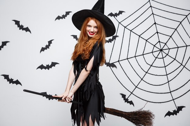 Концепция хэллоуина счастливая элегантная ведьма любит играть с метлой хэллоуин над серой стеной