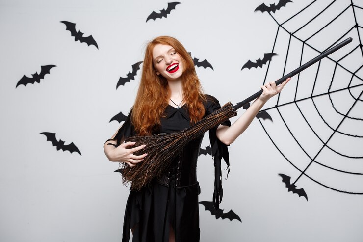 Free Photo halloween concept  happy elegant witch enjoy playing with broomstick halloween party over grey wall