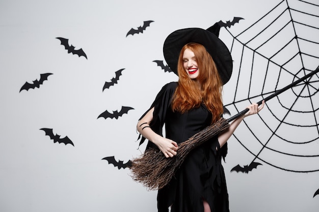 Halloween concept  happy elegant witch enjoy playing with broomstick halloween party over grey wall