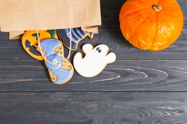 Halloween cookie in paper packet and pumpkin on desk