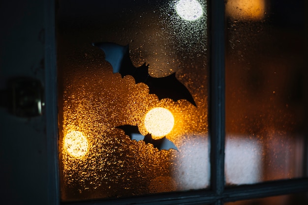 Декоративные летучие мыши на Хэллоуин, застрявшие на окне с каплями дождя