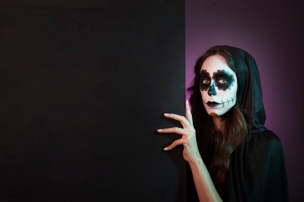 Halloween girl with makeup behind wall