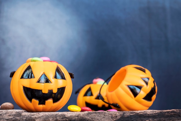 Halloween pumpkin face buckets with colorful candy inside on old wooden plank 