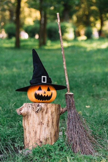 Zucca spettrale di halloween con il cappello sul ceppo vicino al manico di scopa