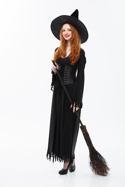 Free photo halloween witch concept  fulllength happy elegant witch with broomstick for celebrating halloween party over white wall