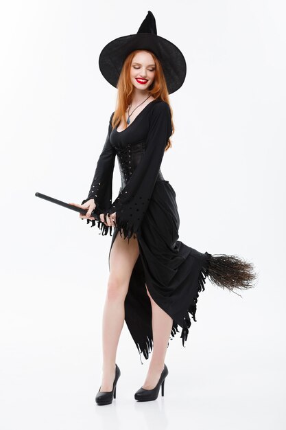 Halloween witch concept  fulllength happy elegant witch with broomstick for celebrating halloween party over white wall