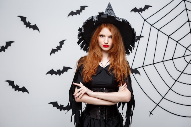 Halloween witch concept  halloween witch holding posing with serious expression over dark grey  wall with bat and spider web