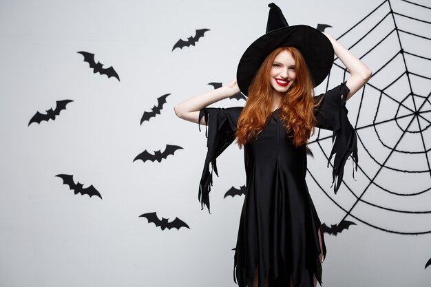 Halloween witch concept  happy halloween witch holding posing over dark grey  wall with bat and spider web