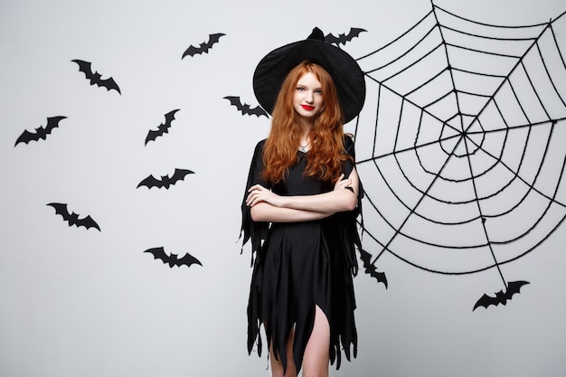 Halloween witch concept  happy halloween witch holding posing over dark grey  wall with bat and spider web