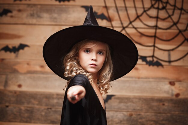 ハロウィーンの魔女のコンセプト小さな魔女の子供は、バットとクモの巣の上の魔法の杖で遊ぶのを楽しんでいます...