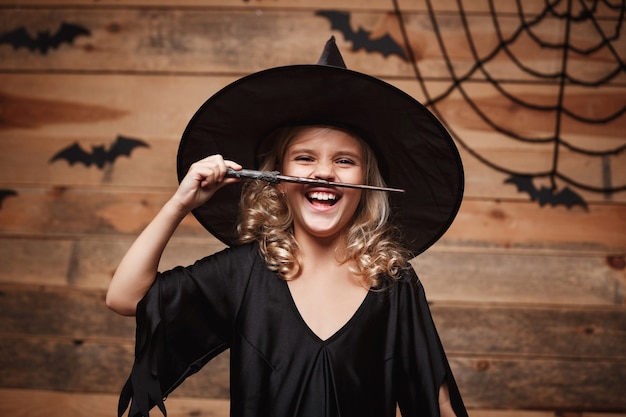 Концепция ведьмы Хэллоуина - маленький ребенок ведьмы любит играть с волшебной палочкой. на фоне летучей мыши и паутины.