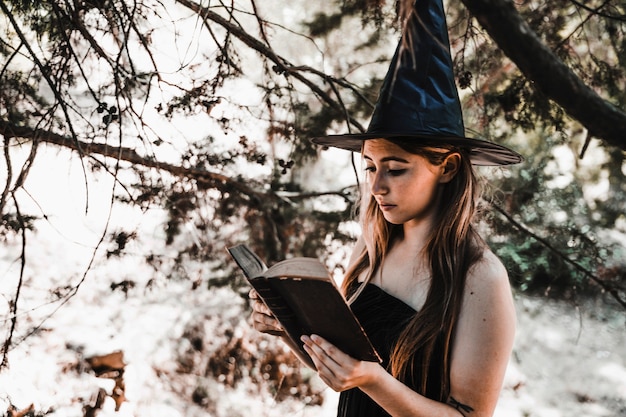 Halloween witch holding old tome in sunny forest