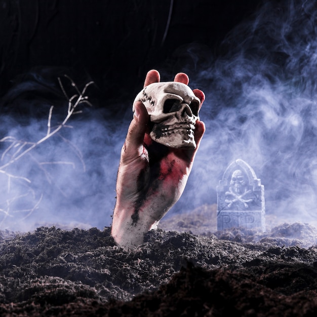 Halloween zombie hand holding skull at cemetery