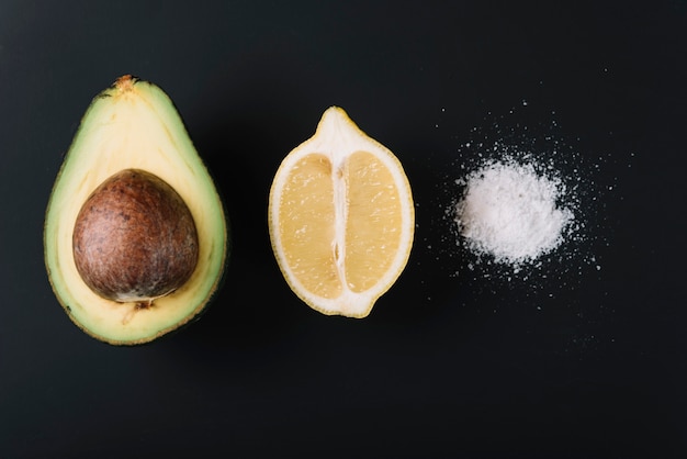 Free photo halved avocado and lemon near salt on black surface