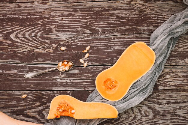 Halved butternut squash and seeds on spoon over the wooden table