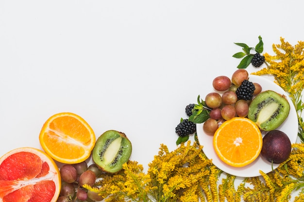 Foto gratuita frutta dimezzata; uva; more e bellissimi fiori gialli su sfondo bianco