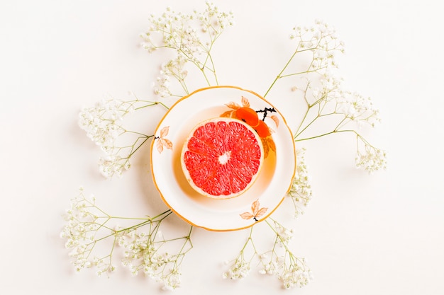 Halved grapefruit on ceramic plate decorated with baby's-breath flowers on white background