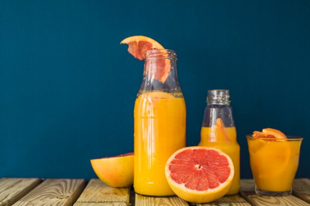 Halved grapefruit and juice in the bottles and glass on table against blue background