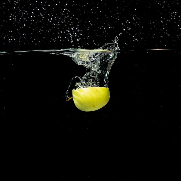 Halved green apple splashing in clear water