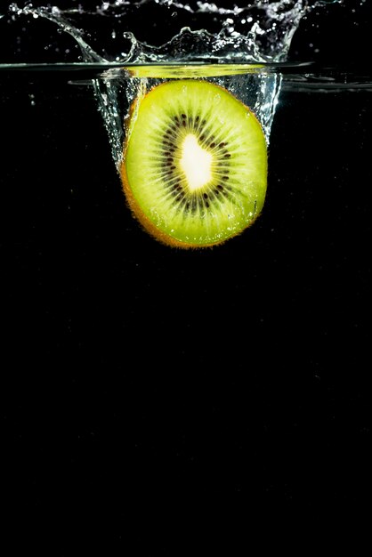 Halved green kiwi splashing in water