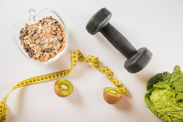 Halved kiwi; measuring tape; oats; dumbbell and lettuce on white surface