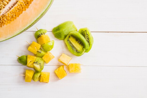 Halved melon with kiwi and pineapple slices on wooden table top