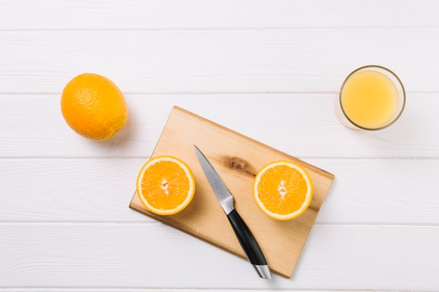 Halved orange on chopping board with glass of juice on white table