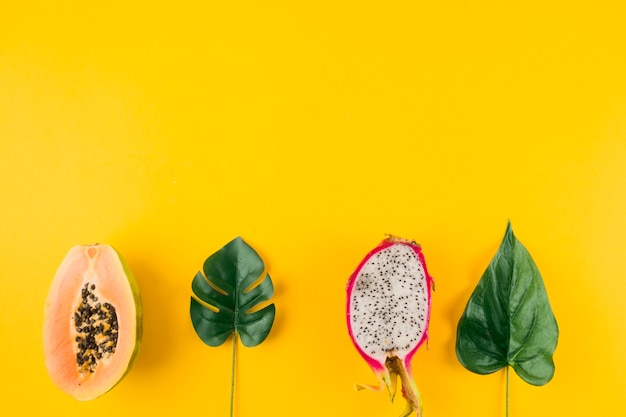 Halved papaya and dragon fruit with artificial leaves on yellow backdrop