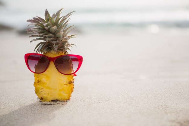 Halved pineapple and a sunglass kept on the sand