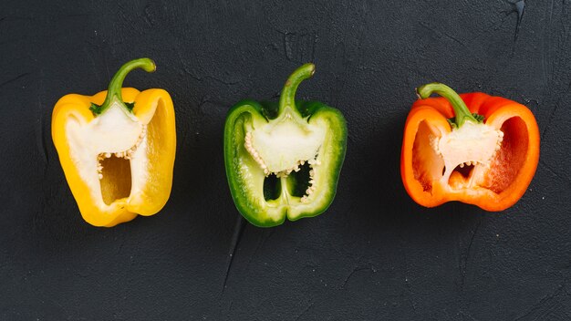 Halved yellow; green and red bell pepper on black concrete textured background