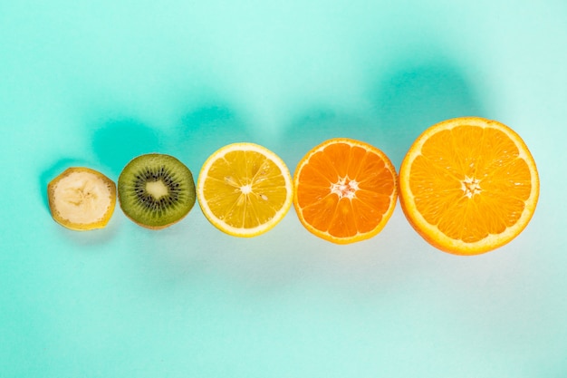 Halves of oranges bananas kiwi and lemons on a blue table