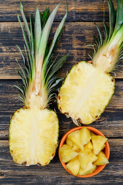 Halves and slices of pineapple in a orange bowl on old wood grunge. flat lay.