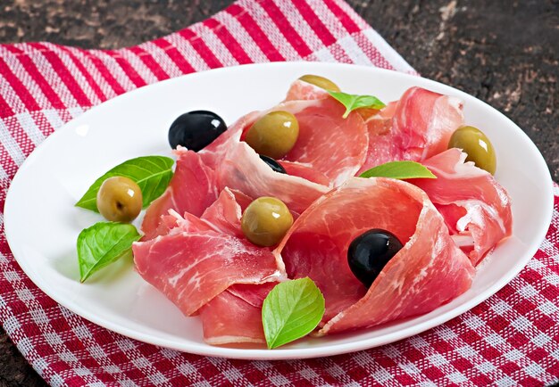 Ham, olives, basil on old wooden