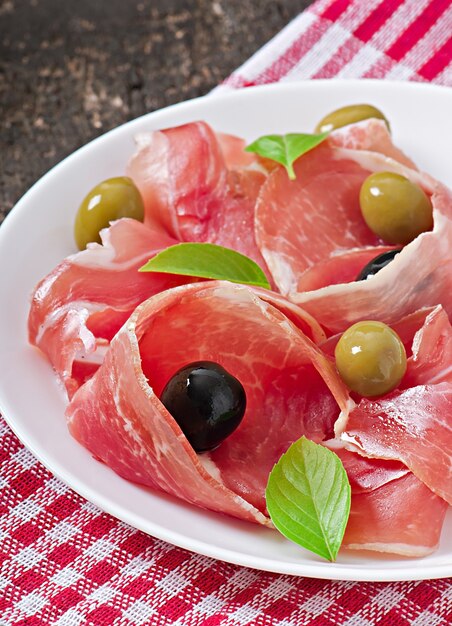 Ham, olives, basil on old wooden