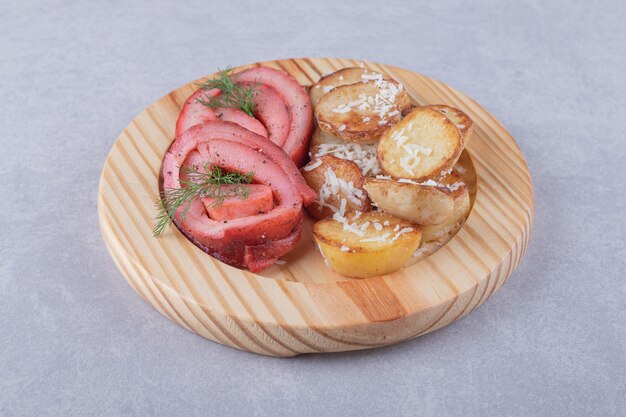 Ham rolls and fried potatoes on wood piece.