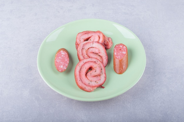 Ham rolls and smoked sausages on green plate. 