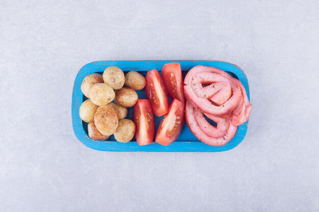 Ham rolls, tomatoes and fried potatoes on blue plate. 