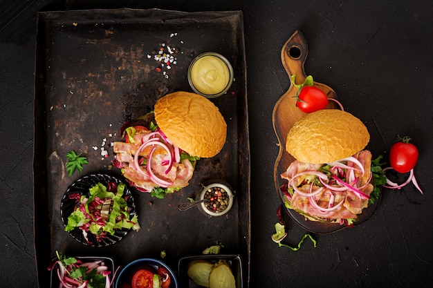 hamburger burger with beef,  tomato, pickled cucumber and fried bacon.