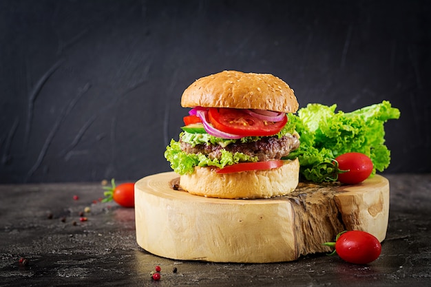 牛肉のハンバーガーと暗いテーブルで新鮮な野菜のハンバーガー。おいしい食べ物。